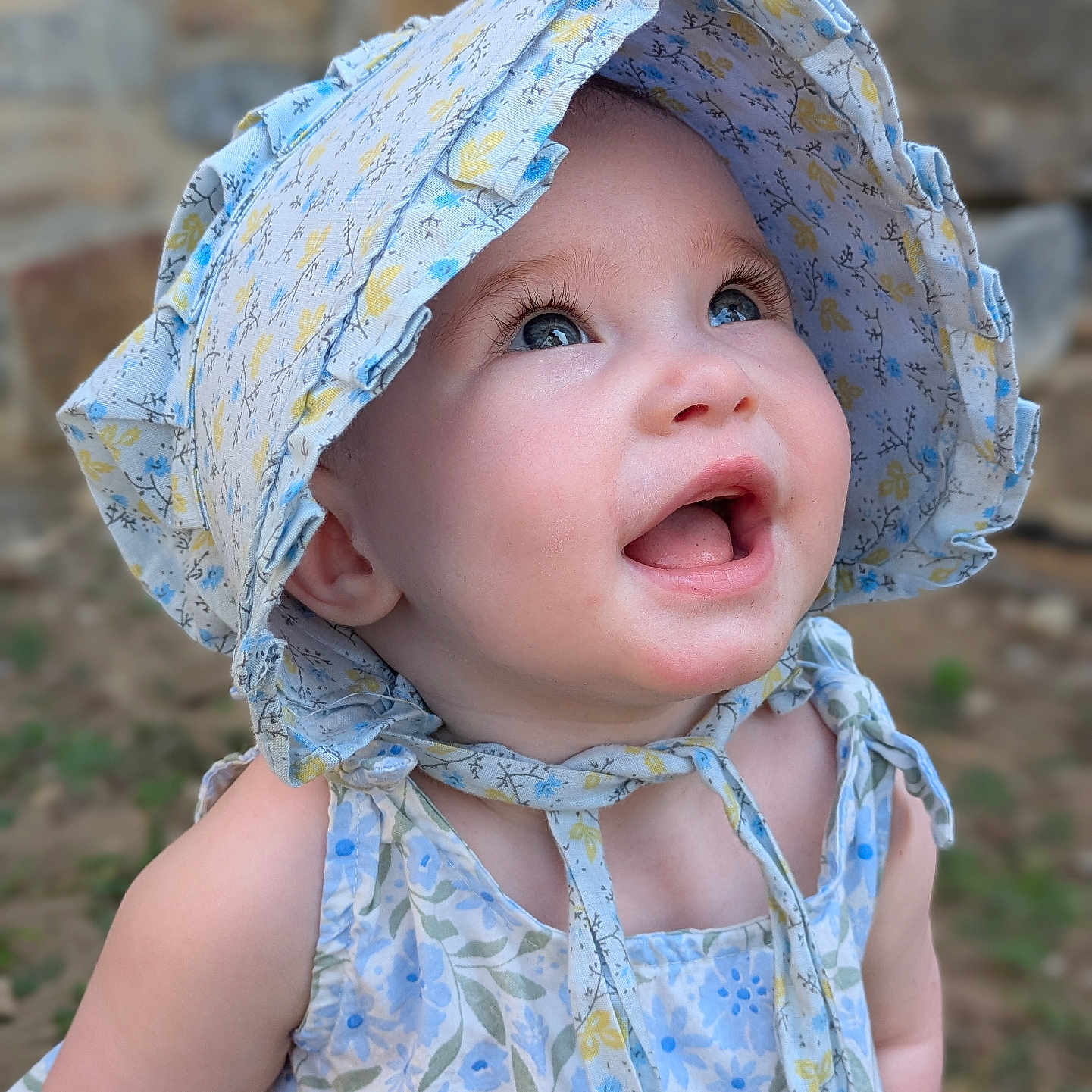 Sofia is registered to the contest to win money with this photo: baby, blue_eyes, bonnet, child, closeup, cute, dress, face, floral_pattern, happy, hat, infant, nature, outdoor, person, portrait, skin, smiling, sunlight, young