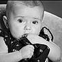 baby, black_and_white, portrait, close_up, infant, child, face, hand, clothing, fabric, sitting, curious, eyes, soft_background, monochrome, cute, young_child, indoor, expression, person