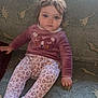 toddler, child, sitting, couch, dinosaur_pattern, sweater, leggings, animal_face, indoor, curly_hair, blue_eyes, cozy, soft_lighting, patterned_fabric, young_child, casual_clothing, portrait, looking_at_camera, home_interior, cute