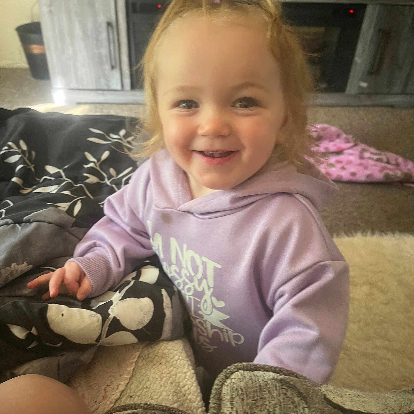 Lila joined the competition — help win amazing prizes! baby, blanket, carpet, child, clothing, cozy, cushion, cute, face, furniture, hair_clip, happy, hoodie, indoor, living_room, person, playful, purple, smiling, toddler