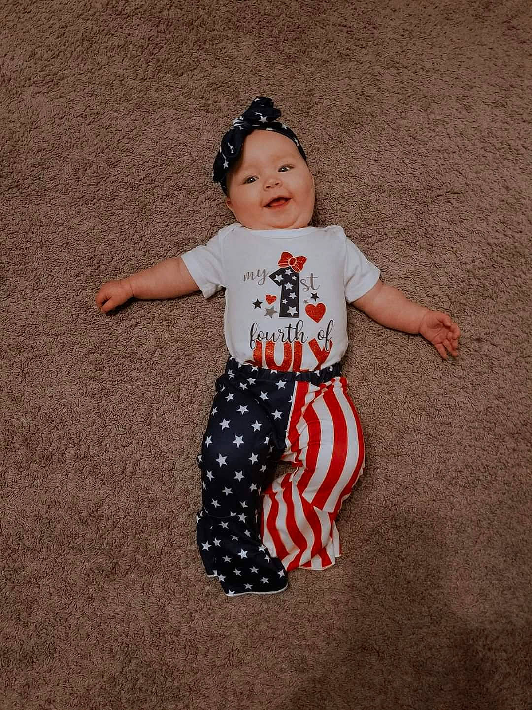 Scarlett is registered to the contest to win money with this photo: arm, art, baby_toddler_clothing, flooring, gesture, happy, headwear, human_body, human_leg, knee, one_piece_garment, outerwear, pattern, person, shoulder, sleeve, smile, sportswear, t_shirt, thigh