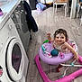 toddler, walker, bubble, kitchen, floor, appliance, washing_machine, cabinet, chair, table, backpack, smiling, happy, indoor, child, toy, flooring, person, home, play