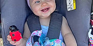 Rosie is registered to the contest to win money with this photo: baby, child, car_seat, smile, headband, toy, duck_toy, colorful_hat, floral_pattern, straps, happy, infant, cute, seatbelt, outdoor, sunlight, hand, clothing, face, portrait
