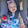 baby, child, car_seat, smile, headband, toy, duck_toy, colorful_hat, floral_pattern, straps, happy, infant, cute, seatbelt, outdoor, sunlight, hand, clothing, face, portrait