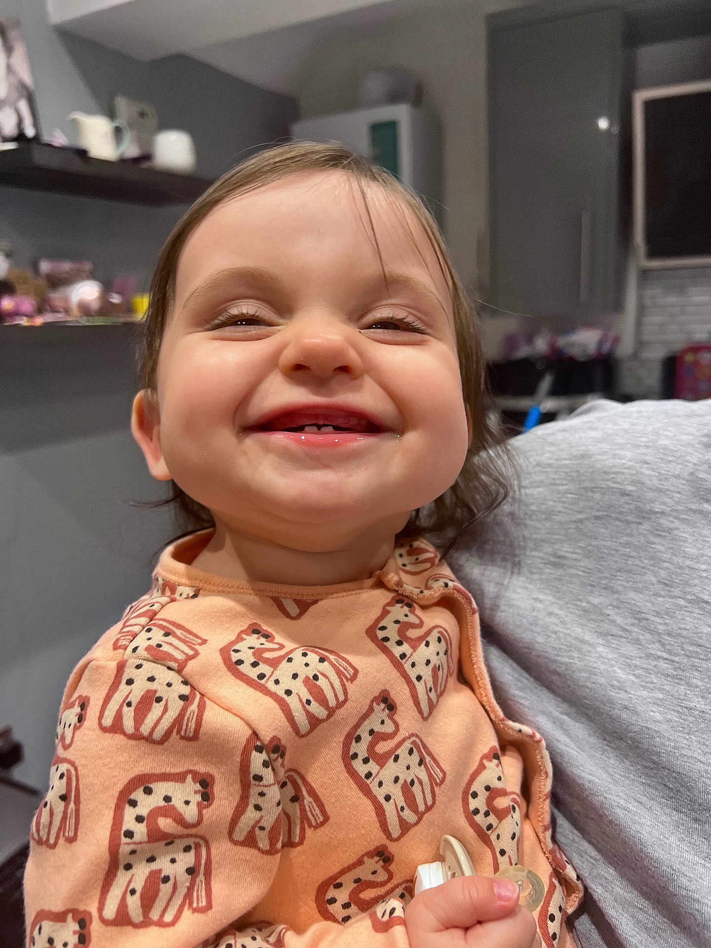 Rosie is registered to the contest to win money with this photo: toddler, smile, child, giraffe_pattern, clothing, indoor, person, cute, happy, baby, holding, pacifier, long_hair, face, head, cheeks, sitting, room, sleeves, casual