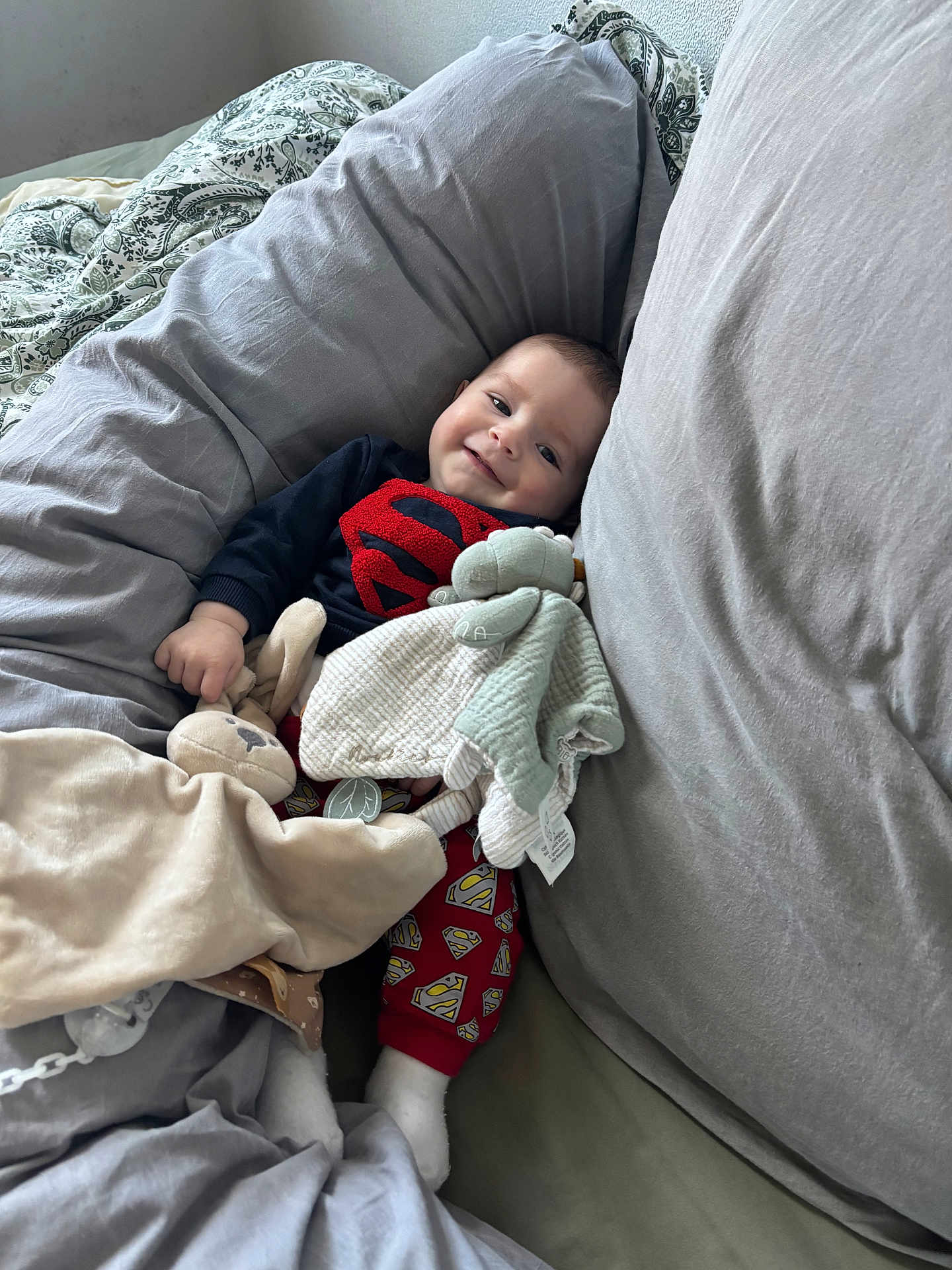 Emilio a rejoint le concours — aidez-le/la à gagner de superbes lots ! baby, superman_outfit, smile, pillow, blanket, stuffed_toy, couch, cozy, child, indoor, cute, red_pants, white_socks, soft_toys, sleeping_area, happy, person, infant, resting, comfort