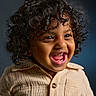 child, toddler, curly_hair, smiling, laughing, beige_shirt, portrait, happy, cute, face, eyes, mouth, teeth, skin, clothing, person, indoor, studio, dark_background, closeup