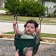 Ezekiel is registered to the contest to win money with this photo: toddler, child, swing, playground, outdoor, park, curly_hair, green_swing, holding_chains, baby, grass, suburban, residential_area, daylight, casual_clothing, person, fun, recreation, seat, play
