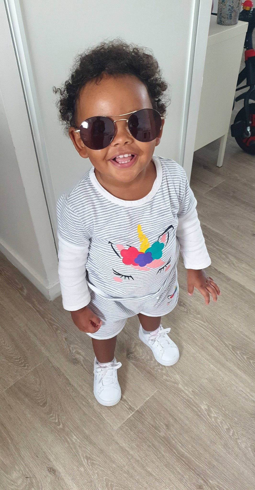 Azély participe au concours pour gagner de l'argent avec cette photo : baby_toddler_clothing, cool, dress, eyewear, face, flooring, glasses, goggles, hair, person, skin, sleeve, smile, standing, sunglasses, t_shirt, tire, toddler, vision_care, white