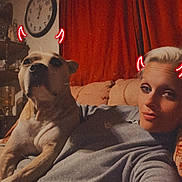 Outlaw is registered to the contest to win money with this photo: person, dog, couch, red_curtains, clock, living_room, selfie, indoors, casual_clothing, pet, filter, neon_horns, relaxing, brown_dog, short_hair, furniture, vintage_filter, warm_lighting, smiling, portrait