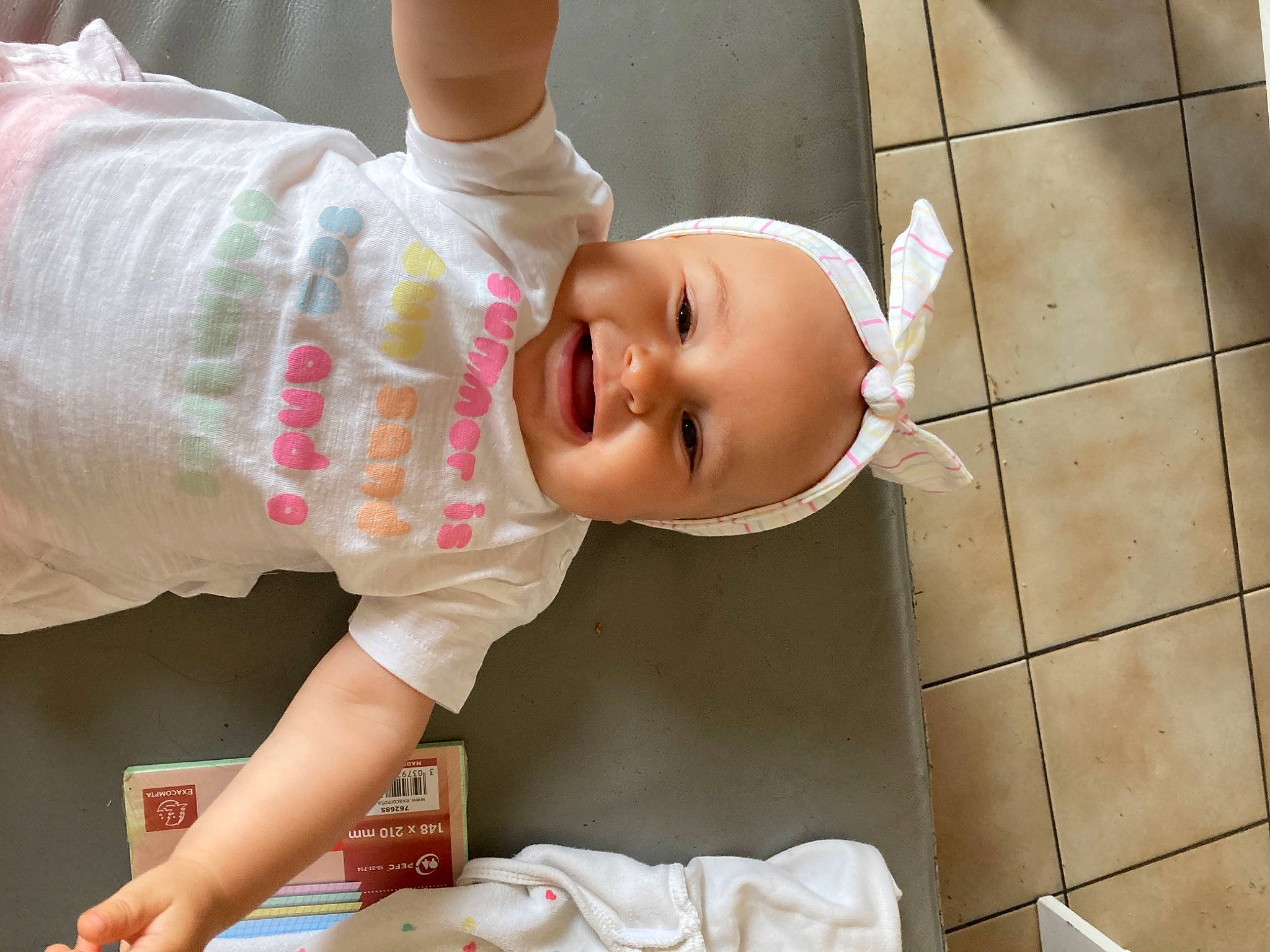 Chloé participe au concours pour gagner de l'argent avec cette photo : baby, baby_products, baby_safety, baby_toddler_clothing, cheek, child, drinkware, flooring, fun, happy, hat, mouth, person, sitting, skin, sleeve, smile, t_shirt, toddler, white
