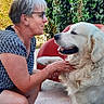 woman, dog, outdoor, garden, ivy, chair, happy, pet, smile, glasses, short_hair, white_dog, fluffy, casual_clothing, greenery, sunlight, interaction, animal, friendship, relaxation