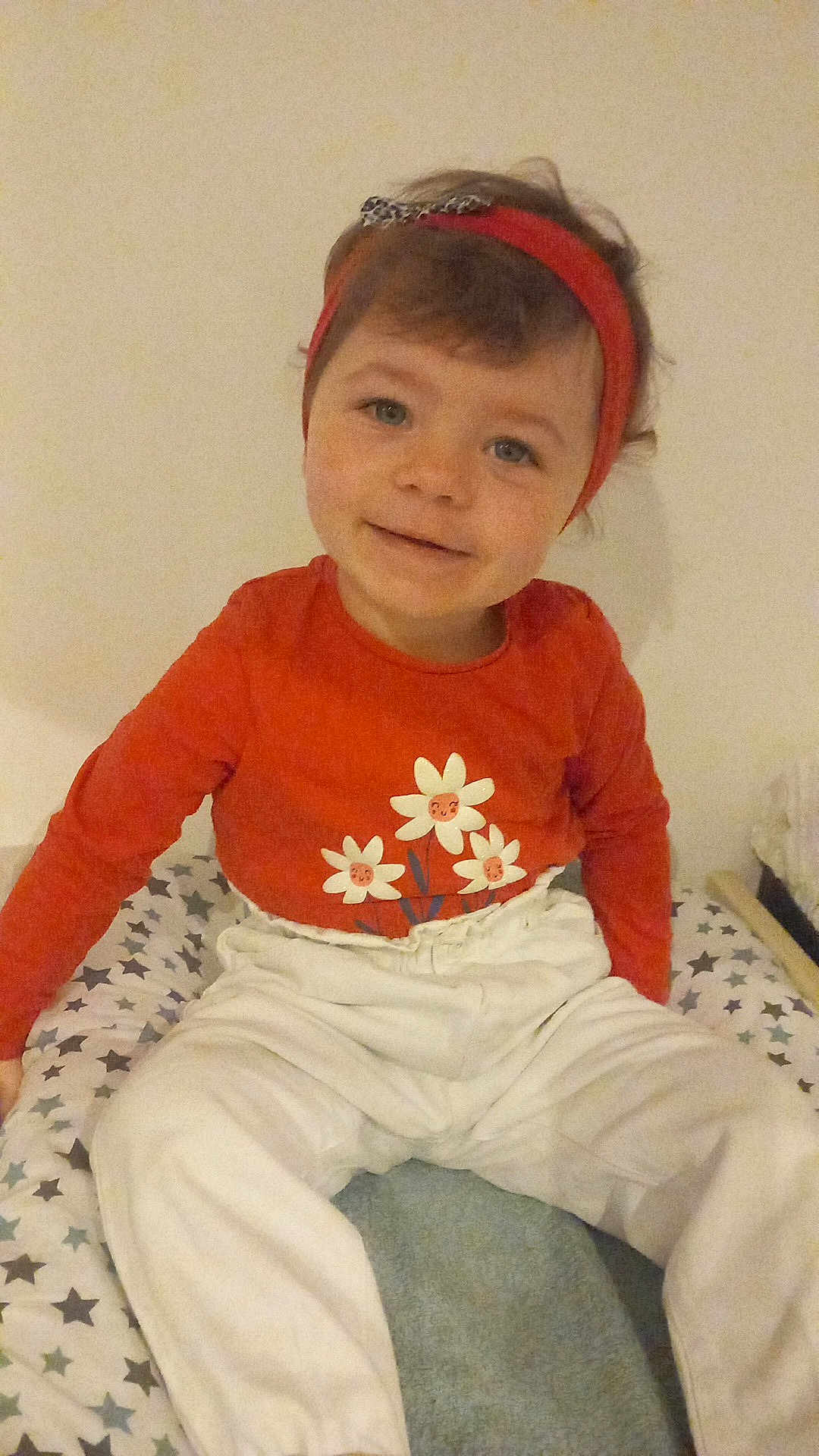 Anna a rejoint le concours — aidez-le/la à gagner de superbes lots ! child, toddler, smiling, headband, red_clothing, white_pants, sitting, indoor, face, person, cushion, patterned, stars, cute, happy, young_child, portrait, casual, baby, expression