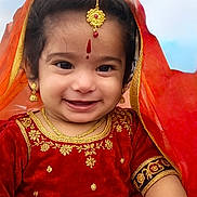 Viha is registered to the contest to win money with this photo: child, toddler, smiling, traditional_clothing, red_dress, gold_jewelry, earrings, necklace, bracelet, headpiece, veil, happy, portrait, face, cute, outdoor, festival, celebration, cultural, young