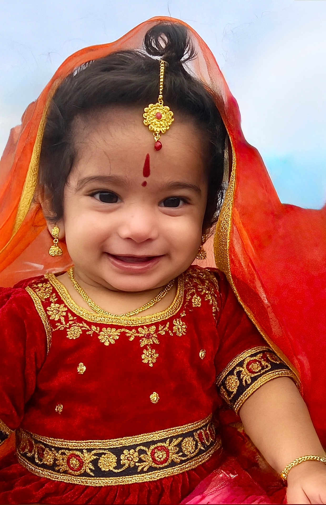 Viha is registered to the contest to win money with this photo: child, toddler, smiling, traditional_clothing, red_dress, gold_jewelry, earrings, necklace, bracelet, headpiece, veil, happy, portrait, face, cute, outdoor, festival, celebration, cultural, young