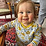 toddler, child, smile, blue_eyes, long_sleeve_shirt, animal_print, indoor, carpet, furniture, chair, person, hand, footwear, floor_tiles, adult, legs, wooden_table, happy, curly_hair, home