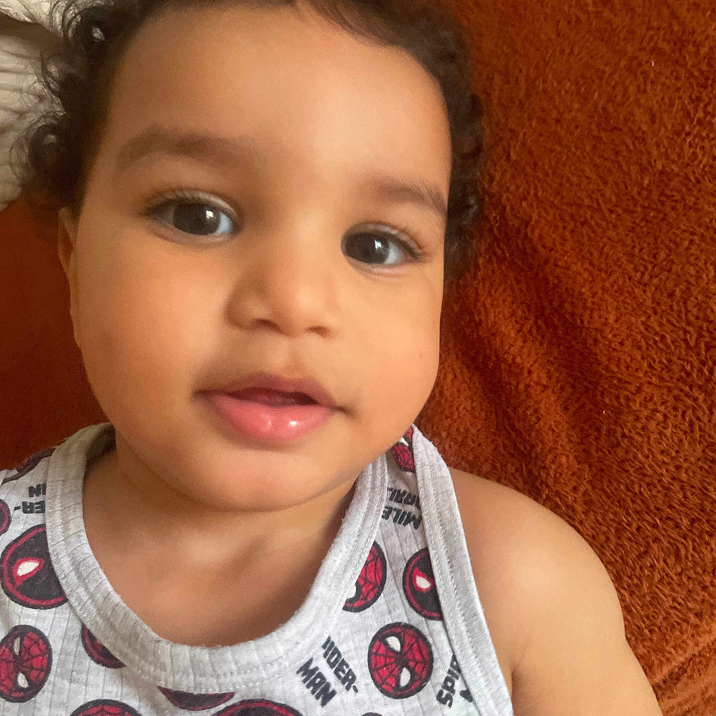 Bayazid a rejoint le concours — aidez-le/la à gagner de superbes lots ! baby, casual, child, closeup, clothing, curly_hair, cute, expression, face, indoors, laying_down, orange_background, person, portrait, skin, smile, spiderman, tank_top, toddler, young_child