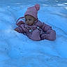 Komani is registered to the contest to win money with this photo: child, baby, snow, winter_clothing, pink_hat, pink_suit, outdoor, forest, trees, cold, winter, snowy_ground, curious, sitting, infant, headwear, nature, seasonal, young_child, cozy