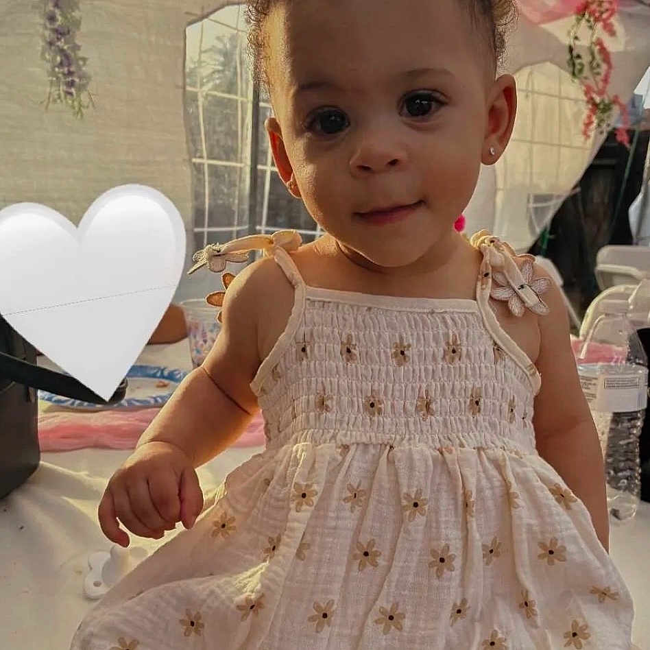 Komani is registered to the contest to win money with this photo: toddler, child, girl, dress, floral, indoors, portrait, cute, curious, earrings, light, soft_light, party_decorations, heart_shape, table, water_bottle, window, smile, skin, hair