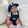 Dylan is registered to the contest to win money with this photo: baby, child, hat, blue_hat, dinosaur_outfit, socks, couch, white_couch, indoors, cute, infant, portrait, sitting, curious, wide_eyes, plush, soft_lighting, casual_clothing, comfortable, smiling_face