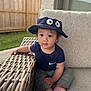 Dylan is registered to the contest to win money with this photo: baby, child, hat, blue_hat, navy_blue, outdoor, sofa, cushion, woven_armrest, fence, grass, curious, sitting, barefoot, casual_clothing, short_sleeve, green_pants, person, portrait, daylight