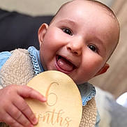 Alba participe au concours pour gagner de l'argent avec cette photo : baby, infant, smiling, happy, holding, wooden_plaque, clothing, vest, denim, face, portrait, cute, closeup, cheerful, child, person, six_months, indoor, fuzzy, celebration