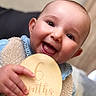 baby, infant, smiling, happy, holding, wooden_plaque, clothing, vest, denim, face, portrait, cute, closeup, cheerful, child, person, six_months, indoor, fuzzy, celebration
