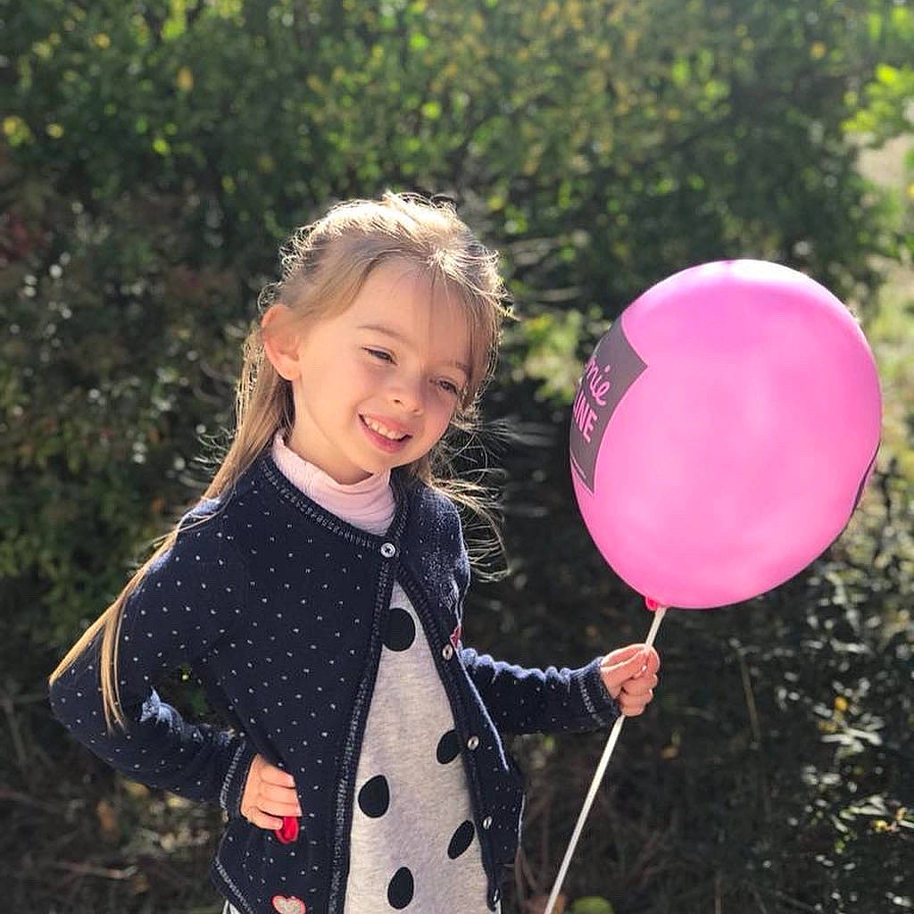 Jessie a rejoint le concours — aidez-le/la à gagner de superbes lots ! baby_toddler_clothing, balloon, child, clothing, face, facial_expression, grass, hair, hairstyle, happy, head, joy, leaf, outerwear, people_in_nature, person, pink, sleeve, smile, standing
