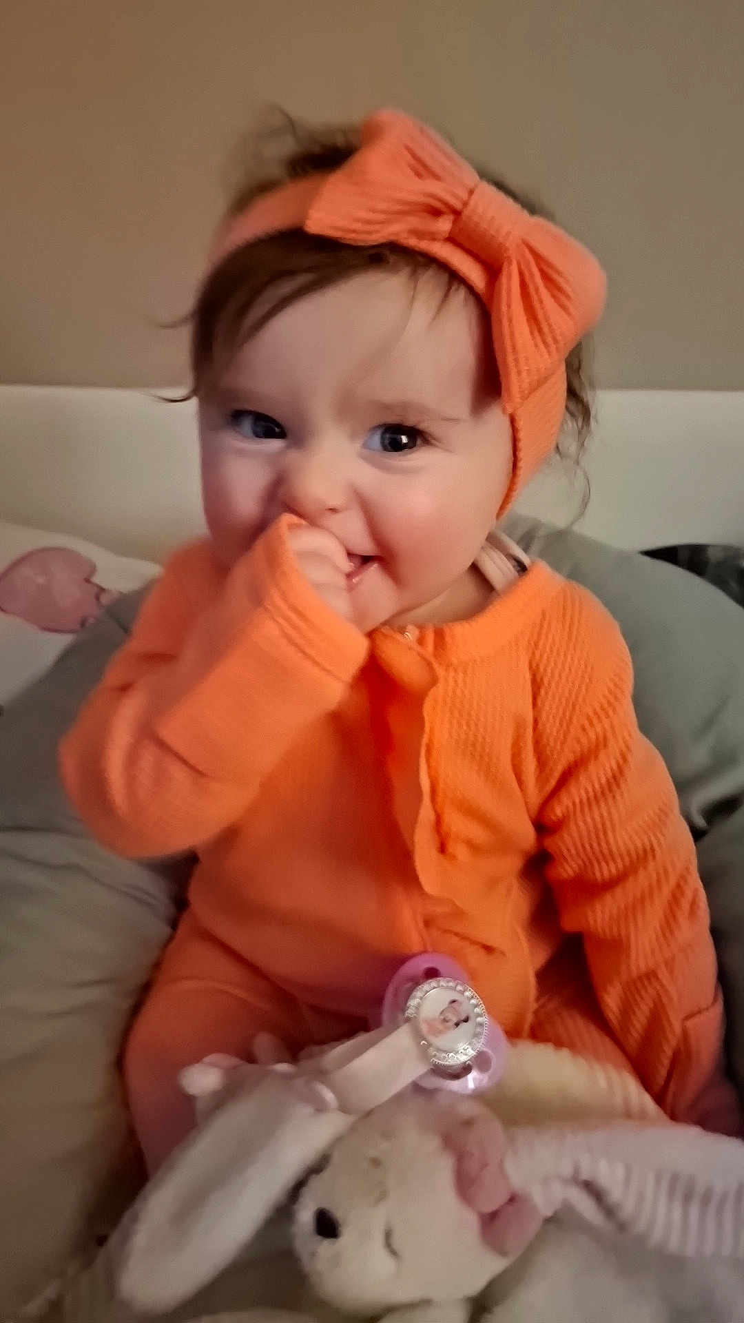 Helyana participe au concours pour gagner de l'argent avec cette photo : baby, infant, toddler, smiling, orange_clothes, headband, bow, pacifier, stuffed_toy, blanket, indoors, portrait, cute, hand_in_mouth, rosy_cheeks, sitting, big_eyes, brown_hair, bed, cozy