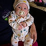 Kayson joined the competition — help win amazing prizes! baby, pacifier, onesie, hat, adult_hand, couch, living_room, clothing, pattern, sitting, person, infant, face, comfort, pink_shoes, fabric, casual, indoor, holding, cute