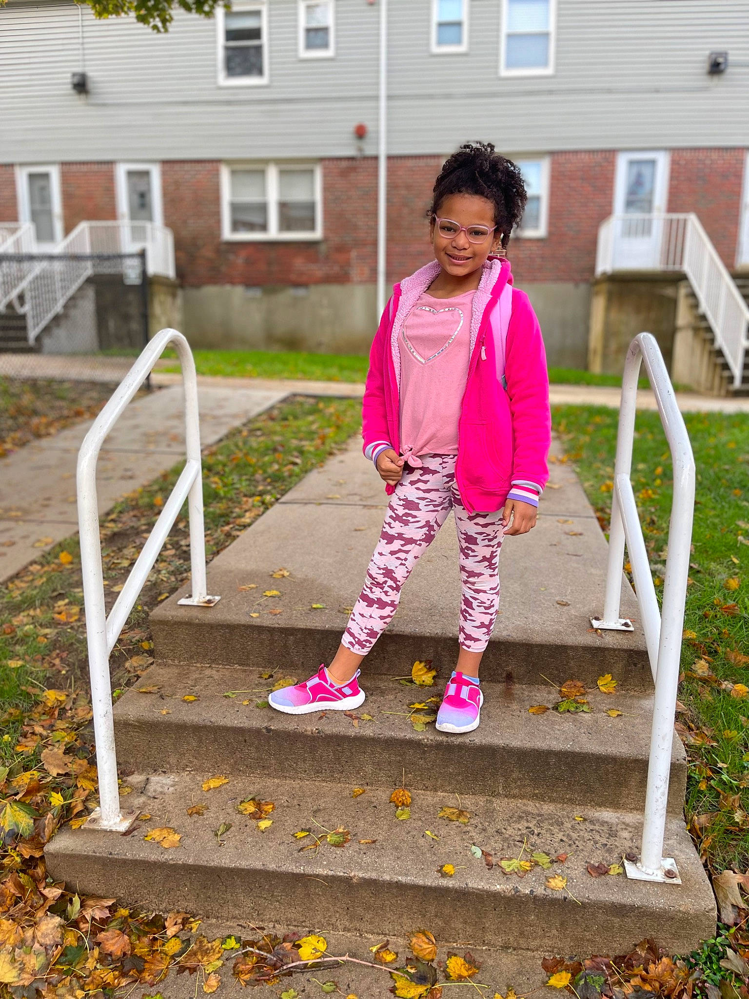 Brianna is registered to the contest to win money with this photo: building, child, city, fun, grass, house, joy, leisure, magenta, outerwear, people_in_nature, person, pink, plant, recreation, road_surface, sidewalk, sleeve, standing, toddler