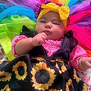 Candace is registered to the contest to win money with this photo: baby, infant, child, headband, bow, sunflower_dress, colorful_clothing, tulle, rainbow_colors, plush_toys, soft_toys, indoors, portrait, cute, chubby_cheeks, hand, fabric, smiling, cozy, bright_colors