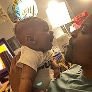 Jonathan is registered to the contest to win money with this photo: baby, adult, man, child, face, smile, balloon, indoor, lamp, television, furniture, clothing, hand, arm, table, container, celebration, joy, interaction, family