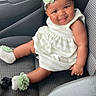 Sernity is registered to the contest to win money with this photo: baby, child, car_seat, infant, smiling, headband, flower_accessory, white_dress, socks, car_interior, seat, cute, portrait, happy, sitting, young_child, person, canned_drink, casual, accessory