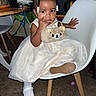 Sernity is registered to the contest to win money with this photo: toddler, child, dress, white_shoes, chair, indoor, plush_purse, cute, curly_hair, hair_bows, carpet, table, furniture, toy, small_handbag, person, smiling, sitting, young_child, curious