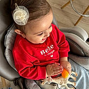 Emili participe au concours pour gagner de l'argent avec cette photo : toddler, child, smiling, red_sweater, toy, giraffe_toy, hair_clip, high_chair, indoor, wooden_floor, happy, cute, baby, clothing, seat_belt, person, playful, hands, face, casual