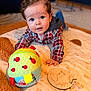 baby, infant, child, face, blue_eyes, plaid_shirt, hoodie, toy_ball, wooden_plaque, milestone_marker, blanket, play_mat, crawling, hand, smile, cozy, indoors, bokeh, soft_toy, portrait