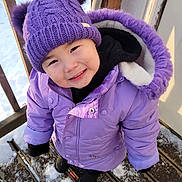 Freya is registered to the contest to win money with this photo: child, toddler, smiling, purple_hat, winter_jacket, snow, outdoor, wooden_deck, cold_weather, skis, gloves, cute, winter_clothing, happy, face, headwear, footwear, playful, person, seasonal
