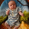 baby, infant, child, striped_clothing, romper, blanket, colorful_blanket, fuzzy_texture, sitting, indoors, cute, small_hands, bare_feet, wood_floor, furniture, curious, portrait, young_child, comfortable, warm