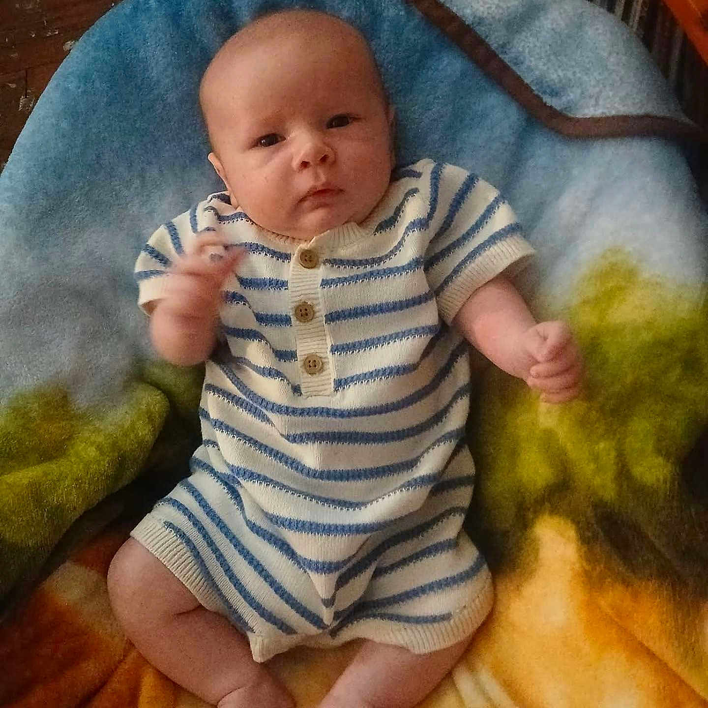 Michael joined the competition — help win amazing prizes! baby, infant, child, striped_clothing, romper, blanket, colorful_blanket, fuzzy_texture, sitting, indoors, cute, small_hands, bare_feet, wood_floor, furniture, curious, portrait, young_child, comfortable, warm