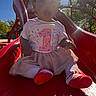 Xamira is registered to the contest to win money with this photo: baby, child, slide, playground, outdoor, sunlight, skirt, shirt, number_one, socks, red, white, curly_hair, expression, seated, fun, daytime, trees, park, toy
