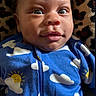 baby, blanket, blue_onesie, child, closeup, cloud_pattern, curious, cute, eyes, face, happy, heart_emoji, indoors, infant, leopard_print, lying_down, portrait, smiling, soft_texture, sun_pattern