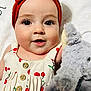 baby, child, face, headband, red_bow, dress, cherry_pattern, stuffed_animal, toy, plush, eyes, skin, mouth, button, fabric, portrait, closeup, infant, cute, smiling