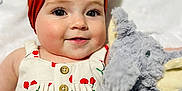 Lyla is registered to the contest to win money with this photo: baby, child, headband, bow, plush_toy, elephant, smile, cherry_pattern, dress, button, face, cute, soft_toy, infant, closeup, portrait, happy, indoor, skin, white_background