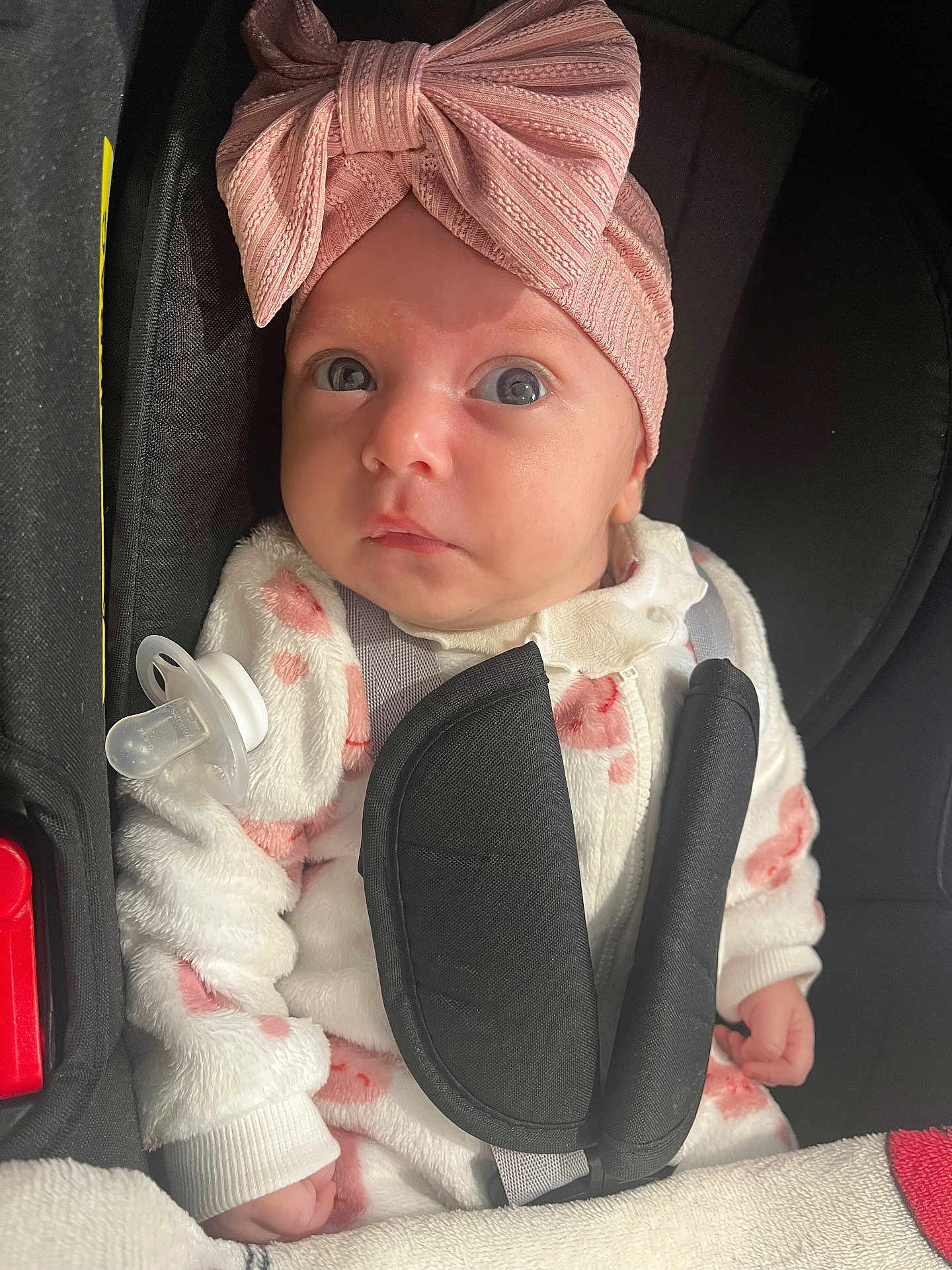 Derine participe au concours pour gagner de l'argent avec cette photo : baby, car_seat, child, close_up, cozy, cute, fabric, hands, headband, indoors, infant, looking_up, pacifier, pink_bow, pink_pattern, portrait, seatbelt, soft_lighting, white_outfit, wide_eyes