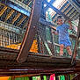 child, indoor_playground, netting, mesh, play_structure, blue_clothing, young_child, grip, looking_down, colorful_background, wall_painting, play_area, wooden_structure, safety_mesh, feet, shorts, toddler, playground_equipment, indoor, active