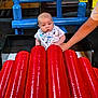 Rohan joined the competition — help win amazing prizes! baby, child, dinosaur_bib, red_instrument, xylophone, blue_chair, hand, play_area, indoor, wooden_structure, colorful, seated, supporting_hand, curious_expression, infant, toy, playground, bright_colors, young_child, person