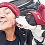 affection, animal, black_and_white_dog, car, casual, close_up, clothing, dog, friendship, happy, hat, headwear, licking, outdoor, person, pet, red_hat, smiling, trunk, winter_hat