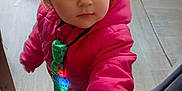 élyna a rejoint le concours — aidez-le/la à gagner de superbes lots ! casual_clothing, child, colorful, curious, floor, furniture, hand, home, indoors, light_up_tie, looking_up, person, pink_jacket, portrait, small_person, standing, toddler, toy, wooden_floor, young_child