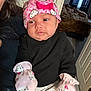 baby, child, infant, person, hat, mittens, pink, hello_kitty, clothing, indoor, holding, black_top, curious, cute, face, headwear, sitting, blanket, door, room